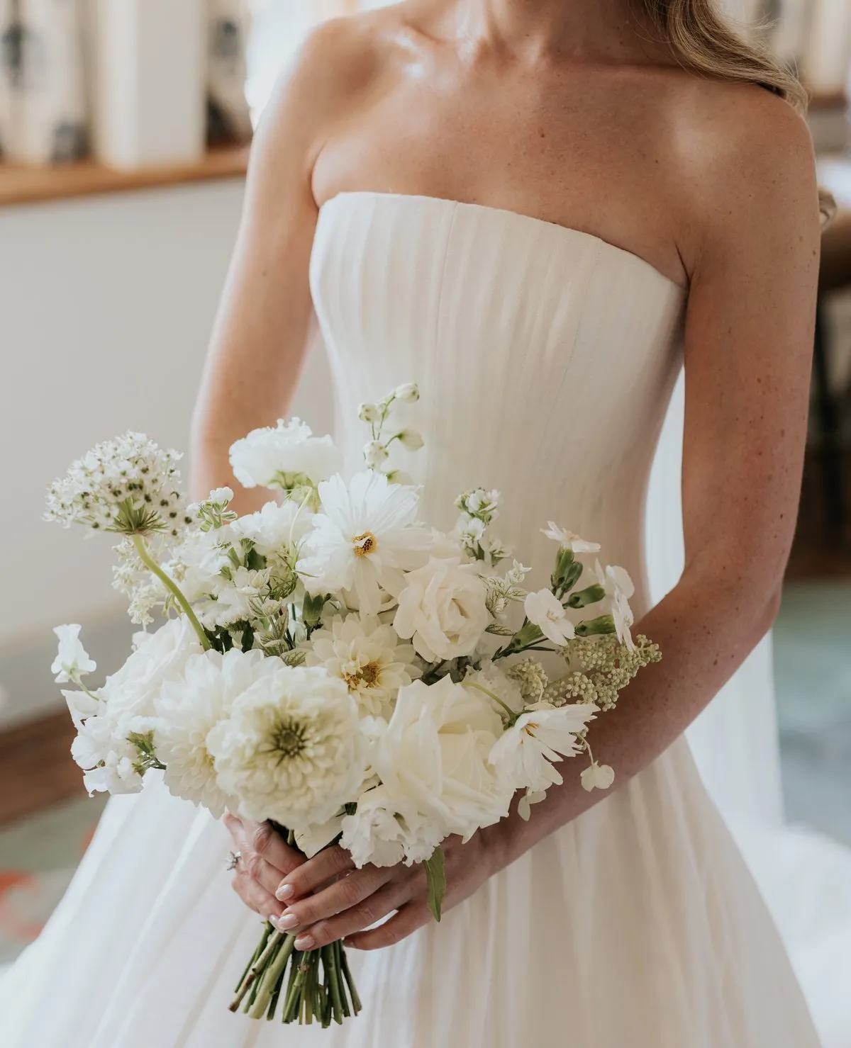 A bride holding a bouquet of white cosmos, dahlias and roses
